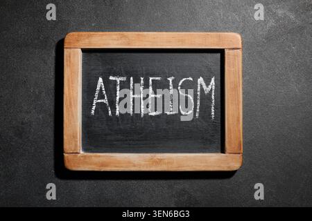 Atheismus-Wort in weißer Kreide auf einer kleinen schwarzen Tafel mit Holzrahmen, dunklem Hintergrund Stockfoto