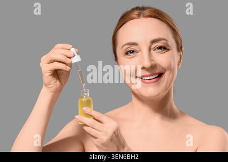 Lächelnde reife Frau, die Gesichtsserum mit Tropfer für Anti-Aging-Hautpflege-Routine und Schönheitsbehandlung aufträgt Stockfoto