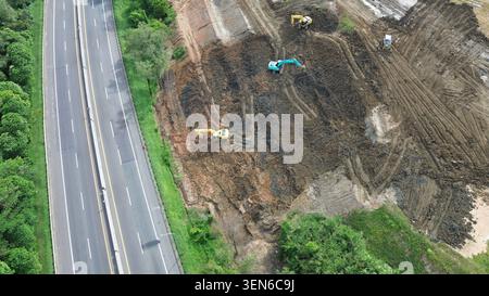 Eine Ansicht von oben nach unten über Erdarbeiten und Aushubarbeiten für ein neues Autobahnbauprojekt mit mehreren Baggern in Indonesien. Stockfoto