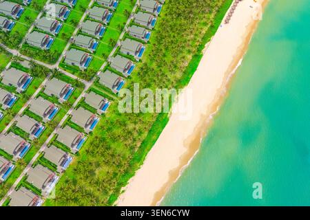 Blick von oben auf viele identische Gebäude mit Gärten, die dicht am Meer am Strand gebaut sind. Häuser Küste mit Kokospalmen und weißem Sand in cr Stockfoto