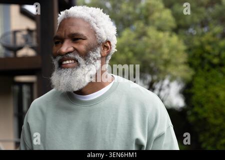 Ranghoher Afroamerikaner posiert auf der Veranda, trägt hellgrünen Rundhalsausschnitt und ein weißes T-Shirt lächelnd Stockfoto