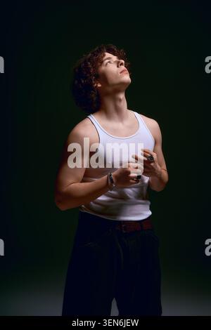 Ein hübscher junger Mann mit lockigen Haaren schaut mit tiefer Emotionen auf, während er modisch gekleidet ist. Stockfoto