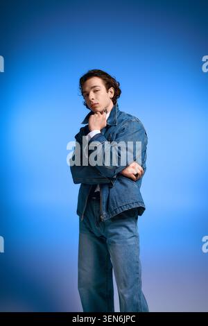 Ein junger Mann mit lockigen Haaren und modischer Jeansbekleidung drückt tiefe Emotionen unter blauer Beleuchtung aus. Stockfoto