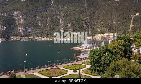 Erhöhter Blick auf die Gärten am Wasser und den Hafen von Riva del Garda am Gardasee, Italien, mit den Berghängen des Monte Baldo über den See. Stockfoto