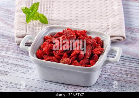 Getrocknete rote Goji-Beeren in weißer Keramikschale mit Minzblättern auf Holztisch Stockfoto
