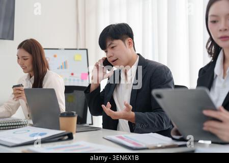 Asiatischer Mann telefoniert mit Geschäftsleuten, die in einem modernen Büro für Kommunikation und Produktivität arbeiten Stockfoto