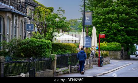 Person (Rückansicht) und Hund im Zentrum von Addingham (vorbei an attraktiven traditionellen Steinhäusern) - Main Street, West Yorkshire, England, Großbritannien. Stockfoto