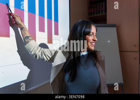 Geschäftsfrau hält eine Unternehmenspräsentation, zeigt selbstbewusst mit einem Stift auf ein projiziertes Balkendiagramm und diskutiert Wachstum und Ergebnisse Stockfoto