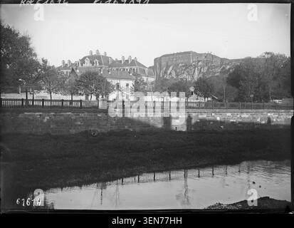 Das Fort und die Burg von Belfort überblicken den Savoureuse River auf diesem Pressefoto von 1920. Die Szene zeigt den Löwen von Belfort und betont die befestigte Architektur, die mit der Stadt verbunden ist. Stockfoto
