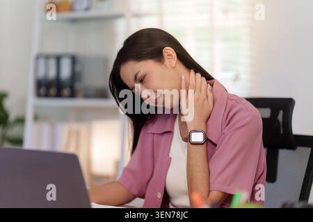 Asiatische Frau mit Nackenschmerzen während der Arbeit am Laptop im Büro für Gesundheit und Ergonomie am Arbeitsplatz Stockfoto