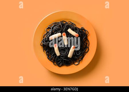 Halloween kreative italienische schwarze Pasta Tintenfisch Tinte verziert lustige Finger auf orangefarbenem Hintergrund. Blick von oben. Lebensmittelkonzept. Stockfoto