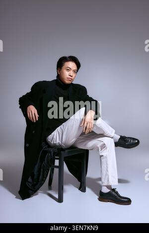 Ein junger asiatischer Mann posiert selbstbewusst in einem Studio und zeigt seinen trendigen Mode-Stil. Stockfoto