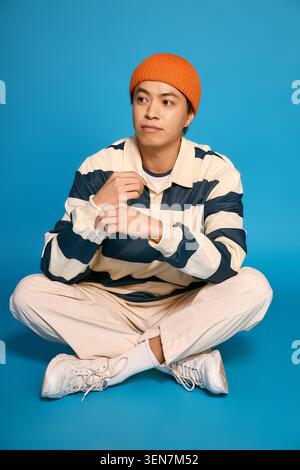 Ein junger asiatischer Mann in einer orangefarbenen Mütze und Streifen zeigt seine einzigartige Mode im Studio. Stockfoto