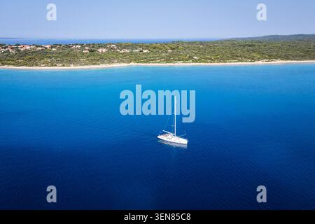 Eine Drohne aus der Luft, die ein einsames weißes Segelboot auf dem pulsierenden blauen Wasser der Adria in der Nähe der Küste der Insel Silba, Kroatien, fängt Stockfoto