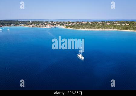 Eine Drohne aus der Luft, die ein einsames weißes Segelboot auf dem pulsierenden blauen Wasser der Adria in der Nähe der Küste der Insel Silba, Kroatien, fängt Stockfoto