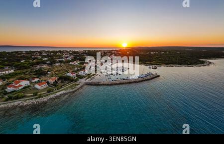 Eine atemberaubende Drohnenaufnahme, die den warmen goldenen Sonnenuntergang über dem Hafengebiet von Mulj auf der Insel Silba, Kroatien, einfängt. Die Perspektive zeigt die Stockfoto