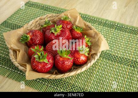 Frische, reife rote Erdbeeren mit grünen Blättern in einem gewebten Korb auf grünem Tischset Stockfoto