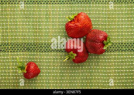 Vier frische, reife rote Erdbeeren auf einer grünen gewebten Matte. Stockfoto
