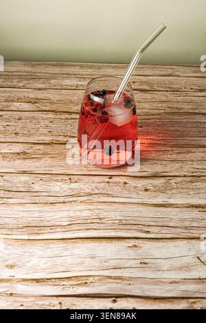 Erfrischendes Getränk aus roten Beeren mit Eiswürfeln und Glasstroh auf einem rustikalen Holztisch mit großzügigem Kopierraum. Stockfoto