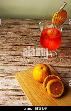Erfrischende Orangenspritze serviert mit Eiswürfeln und frischen Orangenscheiben auf einem rustikalen Holztisch, fotografiert im vertikalen Format. Stockfoto