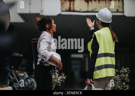 Bauingenieurinnen diskutieren über die Bauinspektion auf einer städtischen Baustelle, während sie Sicherheitsausrüstung tragen Stockfoto