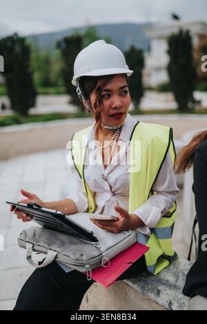 Bauingenieurin in Schutzhelm und Warnweste mit Tablet und Smartphone im Freien Stockfoto