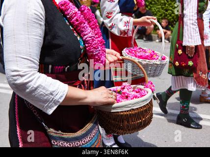 Eine Frau in traditioneller Kleidung hält Körbe, die mit rosa Rosenblüten gefüllt sind, während einer Kulturfestival-Parade auf einer belebten Straße Stockfoto