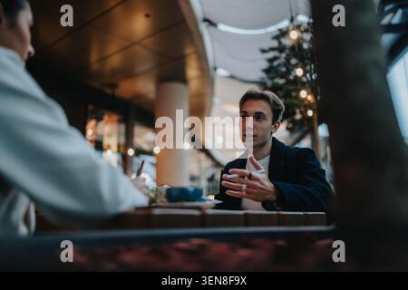 Ein junger Mann, der während eines Geschäftstreffens bei Kaffee in einem modernen Café ein ernsthaftes Gespräch führt Stockfoto