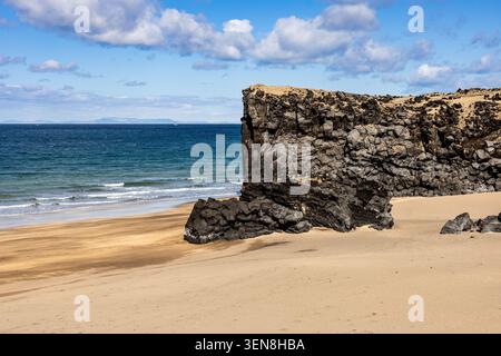 Große Basaltmeerklippe, die sich über Sandstrand an der isländischen Küste erhebt Stockfoto