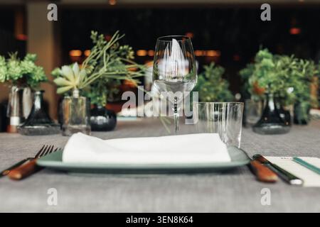 Elegantes Tischgestell für gehobene Küche. Glaswaren glänzen neben der frischen Leinenserviette. Pflanzen verleihen der Szene ein weiches, natürliches Ambiente. Holz u Stockfoto