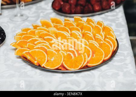 Hellorange Scheiben ordentlich auf einem silbernen Tablett angeordnet. Auf den Tellern sind frische Erdbeeren und Gläser untergebracht. Weiße Tischdecke mit dezenten Blumenmustern. Stockfoto