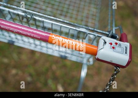 Surrey, England - 6. Juni 2026 - Nahaufnahme eines Sainsbury's Shopping Trolley Griffs mit Münzschloss-System, verlassen in einem Wald Stockfoto