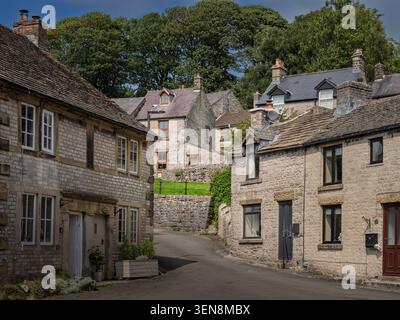 Breiter horizontaler Blick auf die abschüssige Straße des Market Square, gesäumt von traditionellen Kalksteinwohnhäusern im Dorf Tideswell Stockfoto