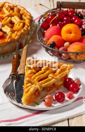 Aprikosenkuchen mit Teigverzierung und einem Metallkorb mit Früchten und Beeren. Stockfoto