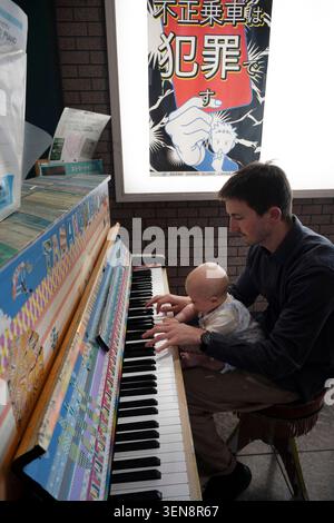 Japan April 2026 UNO Station. Englischer Vater spielt Klavier im Bahnhof, während er auf einen Zug wartet Stockfoto
