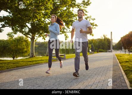 Lächelnde junge Joggingtour im Park am sonnigen Tag, aktive gesunde Lebensweise Stockfoto