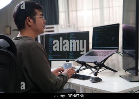 Ein Entwickler, der sich mit der Programmierung beschäftigt und mehrere Monitore verwendet, die Code anzeigen und so eine produktive Codierungsumgebung hervorheben. Stockfoto