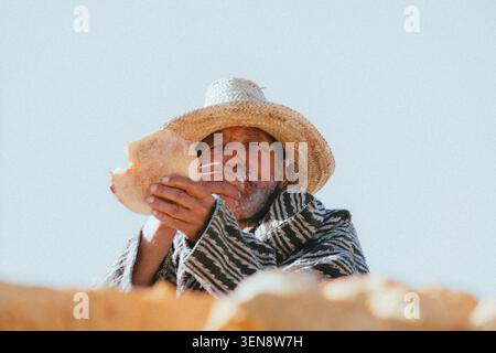 Marokkanischer Mann in traditioneller Djellaba und Strohhut essen Brot Stockfoto