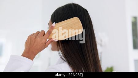 Frau, die Haare putzt und Haarpflege zu Hause mit Rücken, Morgenroutine und Pflege im Badezimmer. Bambusbürste, weibliche Person und Selbstpflege zu Hause Stockfoto