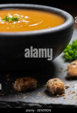 Cremige Kürbissuppe in einer dunklen Schüssel, garniert mit frischer Petersilie und serviert mit knusprigen Croutons. Warme, angenehme Herbstmahlzeit in sattem Orange Stockfoto