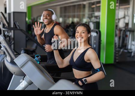 Lächelnder junger Schwarzer, der beim Training auf Laufbändern in einem modernen Fitnessstudio winkt Stockfoto