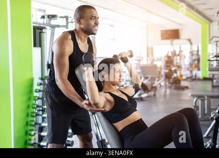 Personal Trainer, der junge Frau beim Neigungsmanteldrücken im Fitnessstudio betreut Stockfoto