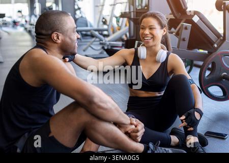 Junger Schwarzer, der sich nach dem Training in einem modernen Fitnessstudio entspannt und redet Stockfoto