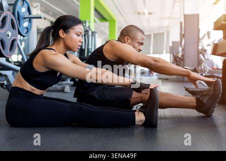 Schwarze Fitness, die sich vor oder nach dem Workout auf dem Fitnessboden ausdehnt Stockfoto