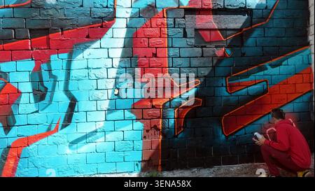 Stockholm, Schweden, 17. Mai 2026. Ein Straßenkünstler malt ein leuchtendes blau-rotes Graffiti-Wandgemälde auf einer strukturierten Ziegelwand, das urbane Kreativität zum Ausdruck bringt, b Stockfoto