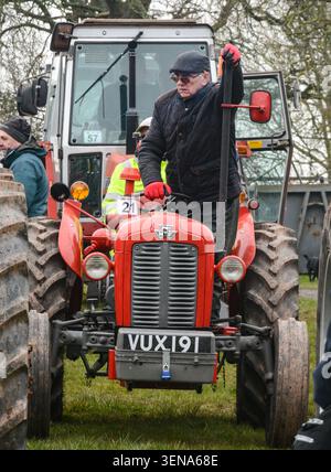 Ein Mann, der auf einem alten Traktor steht und den warmen Auspuff bei einem Event im Freien spürt und klassische Landmaschinen und das ländliche Erbe erfasst Stockfoto