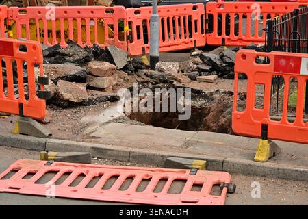 Ausgegrabenes Straßenloch, umgeben von orangen Sicherheitsbarrieren und Schutt Stockfoto