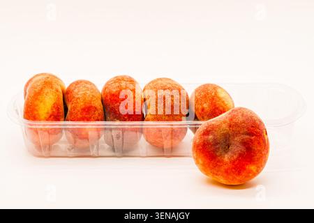 Köstliche und gesunde süße Frucht flache Pfirsiche in einem Plastikbehälter isoliert auf einem weißen Hintergrund Stockfoto