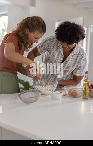 Kombinieren Sie das Mischen von Teig und das Gießen von Flüssigkeit auf der hellen Kücheninsel mit Glasschale Stockfoto