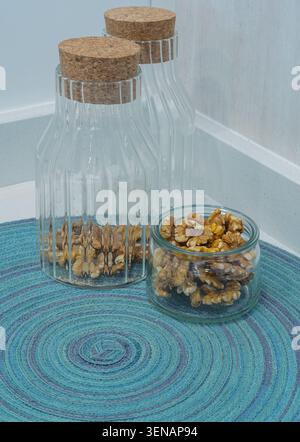 Walnüsse in Glasschale mit dekorativen Küchengläsern auf einer hellblauen Tischdecke Stockfoto